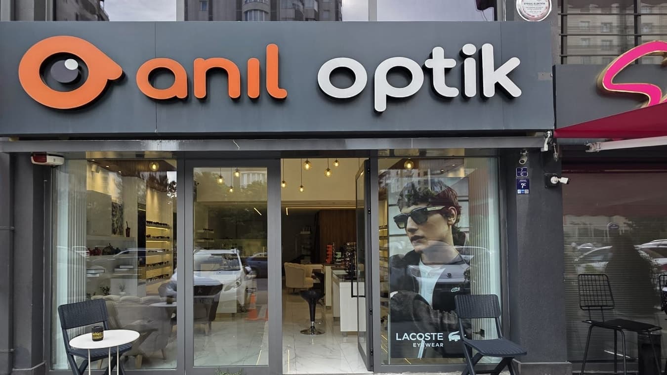 Anıl Optik'in Sevgi Sokak üzerindeki gri cepheli dükkânı; turuncu göz logolu tabelası, cam giriş kapısı ve kaldırımdaki masa-sandalye